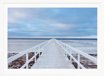 A framed photograph capturing a long, white wooden pier from a central perspective, leading the eye across a calm, icy sea towards the distant horizon under a cloudy blue sky. Print