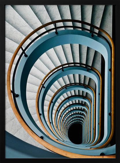 A high-angle, top-down photograph of a multi-story rectangular spiral staircase, creating a hypnotic, receding pattern. The steps are light gray marble, contrasted by shadows, and the balustrade is a striking light blue with a warm wooden handrail, leading down to a dark abyss at the center. Wall Art