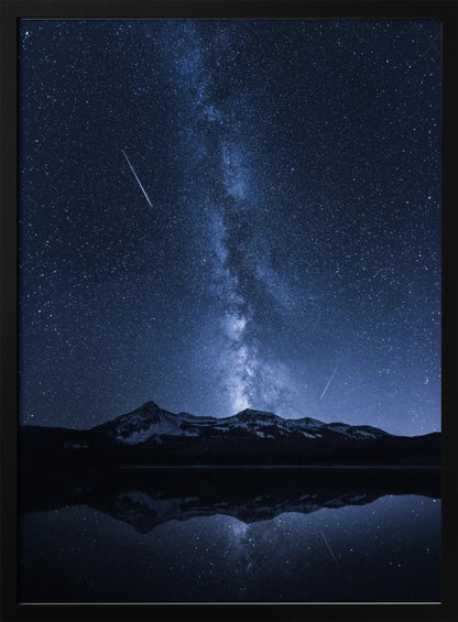 A breathtaking night photograph of the Milky Way galaxy stretching vertically across a deep blue, star-filled sky. Two shooting stars streak through the atmosphere above a dark, snow-dusted mountain range, which is perfectly reflected in the calm, mirror-like surface of a lake in the foreground. Artwork
