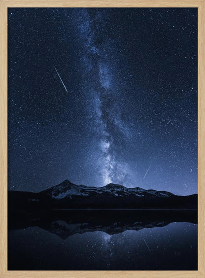 A breathtaking night photograph of the Milky Way galaxy stretching vertically across a deep blue, star-filled sky. Two shooting stars streak through the atmosphere above a dark, snow-dusted mountain range, which is perfectly reflected in the calm, mirror-like surface of a lake in the foreground. Artwork