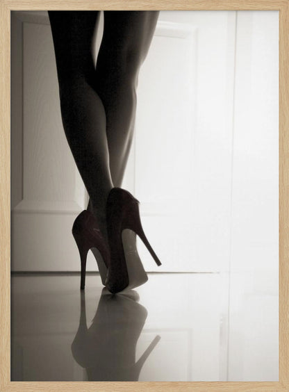 A low-angle, black and white photograph focusing on a woman's legs as she stands with them crossed. She wears dark red stiletto high heels, which cast a clear reflection on the glossy floor. Her legs are silhouetted against a bright white door in the background, creating a dramatic and sensual mood. Decor
