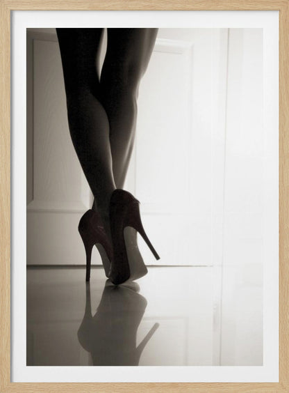 A low-angle, black and white photograph focusing on a woman's legs as she stands with them crossed. She wears dark red stiletto high heels, which cast a clear reflection on the glossy floor. Her legs are silhouetted against a bright white door in the background, creating a dramatic and sensual mood. Decor