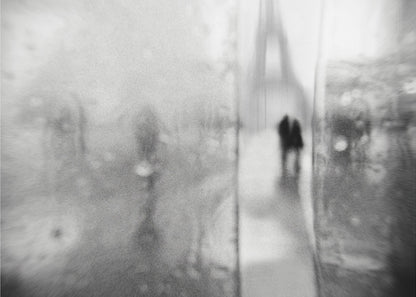 A framed, moody black and white photograph with a heavy blur effect, depicting a couple's silhouette walking towards the distant, hazy Eiffel Tower on what appears to be a rainy day in Paris. Artwork