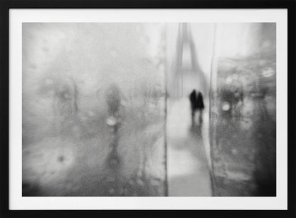 A framed, moody black and white photograph with a heavy blur effect, depicting a couple's silhouette walking towards the distant, hazy Eiffel Tower on what appears to be a rainy day in Paris. Artwork
