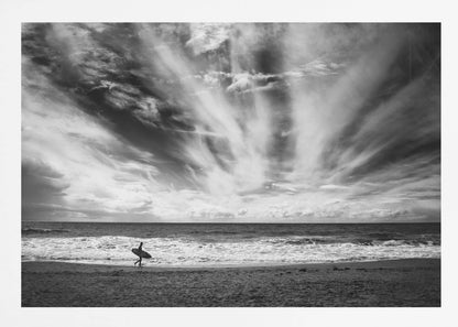 A dramatic black and white photograph of a lone surfer silhouetted against the sea, walking along a sandy beach. The sky is filled with spectacular, radiating clouds that stretch across the horizon, creating a powerful and moody atmosphere. The image is enclosed in a silver frame. Poster