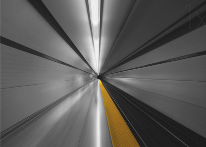 An abstract, long-exposure photograph from a first-person perspective inside a tunnel, creating a motion-blurred effect. The scene is mostly black and white, with lines radiating from a central vanishing point, but a single, bold yellow line runs down the center, adding a pop of selective color. The artwork is presented in a silver frame. Print