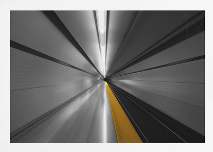 An abstract, long-exposure photograph from a first-person perspective inside a tunnel, creating a motion-blurred effect. The scene is mostly black and white, with lines radiating from a central vanishing point, but a single, bold yellow line runs down the center, adding a pop of selective color. The artwork is presented in a silver frame. Print
