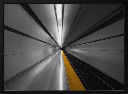 An abstract, long-exposure photograph from a first-person perspective inside a tunnel, creating a motion-blurred effect. The scene is mostly black and white, with lines radiating from a central vanishing point, but a single, bold yellow line runs down the center, adding a pop of selective color. The artwork is presented in a silver frame. Print