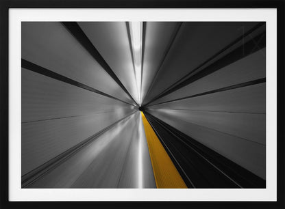 An abstract, long-exposure photograph from a first-person perspective inside a tunnel, creating a motion-blurred effect. The scene is mostly black and white, with lines radiating from a central vanishing point, but a single, bold yellow line runs down the center, adding a pop of selective color. The artwork is presented in a silver frame. Print