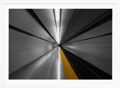 An abstract, long-exposure photograph from a first-person perspective inside a tunnel, creating a motion-blurred effect. The scene is mostly black and white, with lines radiating from a central vanishing point, but a single, bold yellow line runs down the center, adding a pop of selective color. The artwork is presented in a silver frame. Print