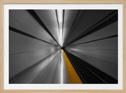 An abstract, long-exposure photograph from a first-person perspective inside a tunnel, creating a motion-blurred effect. The scene is mostly black and white, with lines radiating from a central vanishing point, but a single, bold yellow line runs down the center, adding a pop of selective color. The artwork is presented in a silver frame. Print