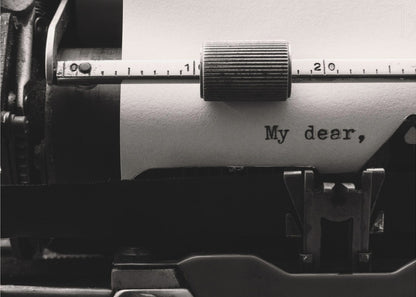 A close-up, black and white photograph of a vintage typewriter. A sheet of white paper is loaded, and the words 'My dear,' have just been typed, creating a sense of nostalgia and romance. The image is enclosed in a silver frame. Wall Art