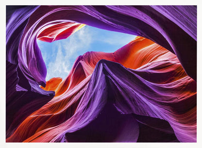 A low-angle photograph looking up from inside a vibrant slot canyon. The smooth, flowing sandstone walls are colored in rich shades of purple, red, and orange, curving around an opening that reveals a bright blue sky with wispy clouds. The image is presented within a silver-colored frame. Wall Art