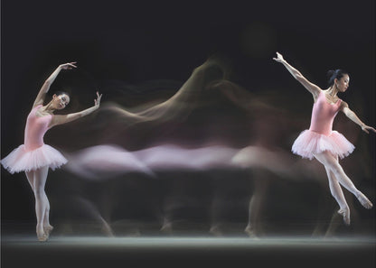 A long-exposure photograph capturing the fluid motion of a ballerina in a pink leotard and tutu. Two clear poses of the dancer frame a central, ethereal blur of movement against a dark, solid background, all encased in a silver frame. Artwork