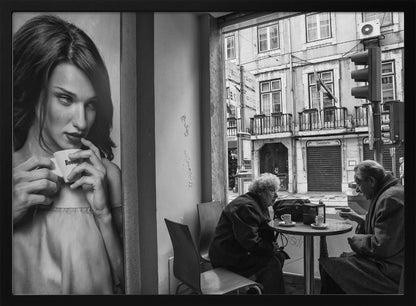 A framed, black and white photograph capturing a scene of juxtaposition. On the left, a large poster shows a glamorous young woman holding a coffee cup. On the right, seen through a cafe window, an elderly couple sits at a small table, also with coffee cups, engaged in conversation against a backdrop of an old European city street. Poster