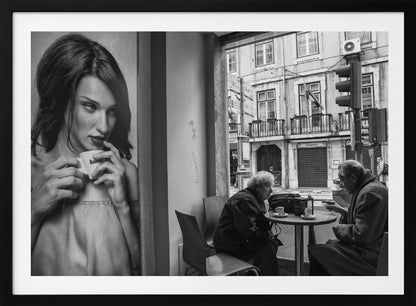 A framed, black and white photograph capturing a scene of juxtaposition. On the left, a large poster shows a glamorous young woman holding a coffee cup. On the right, seen through a cafe window, an elderly couple sits at a small table, also with coffee cups, engaged in conversation against a backdrop of an old European city street. Poster