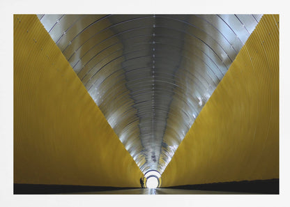 A symmetrical, perspective view down a modern, circular tunnel. The lower walls are bright yellow, creating two diagonal lines that converge towards a bright, white light at the far end. The arched ceiling is made of reflective silver metal panels, and a small silhouette stands near the exit. Artwork