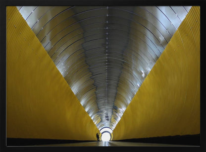 A symmetrical, perspective view down a modern, circular tunnel. The lower walls are bright yellow, creating two diagonal lines that converge towards a bright, white light at the far end. The arched ceiling is made of reflective silver metal panels, and a small silhouette stands near the exit. Artwork