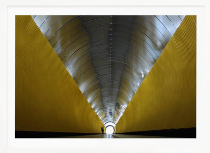 A symmetrical, perspective view down a modern, circular tunnel. The lower walls are bright yellow, creating two diagonal lines that converge towards a bright, white light at the far end. The arched ceiling is made of reflective silver metal panels, and a small silhouette stands near the exit. Artwork