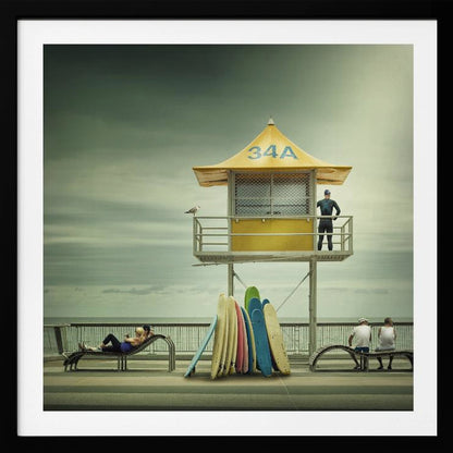 A vintage-style photograph of a yellow lifeguard tower labeled '34A' on a beach boardwalk under an overcast, greenish sky. A lifeguard in a wetsuit stands on the balcony, while a collection of colorful surfboards leans against the base. People are seen relaxing on benches nearby. Print