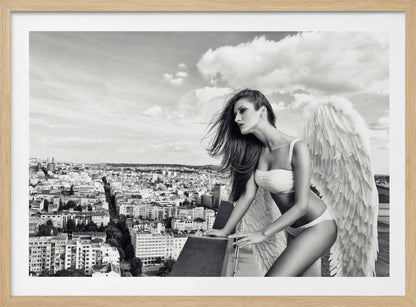 A framed black and white photograph of a woman with large angel wings wearing white lingerie, looking out over a cityscape from a high vantage point. Her long dark hair is blowing in the wind, and the sky is filled with clouds. Poster