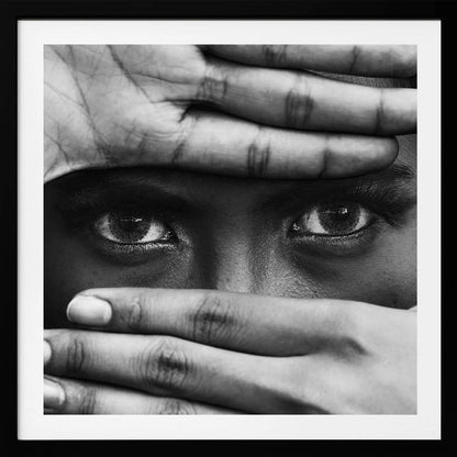A powerful black and white close-up photograph of a person's face, framed in light wood. Their hands cover most of their face, one over the forehead and the other over the mouth, revealing only their intense, striking eyes that gaze directly forward. Print
