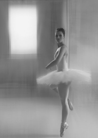 A black and white artistic photograph of a ballerina in a white leotard and tutu, mid-pose on pointe. The image has a motion blur effect, creating a dreamy and ethereal atmosphere as she glances back at the camera. Decor