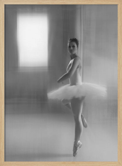 A black and white artistic photograph of a ballerina in a white leotard and tutu, mid-pose on pointe. The image has a motion blur effect, creating a dreamy and ethereal atmosphere as she glances back at the camera. Decor