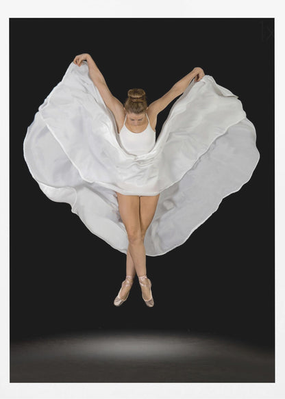 A high-angle studio photograph of a graceful ballet dancer suspended mid-air against a solid black background. She wears a white leotard and pointe shoes, with her legs crossed. Her arms are outstretched, holding a large, flowing white fabric that creates a shape like wings around her. Decor