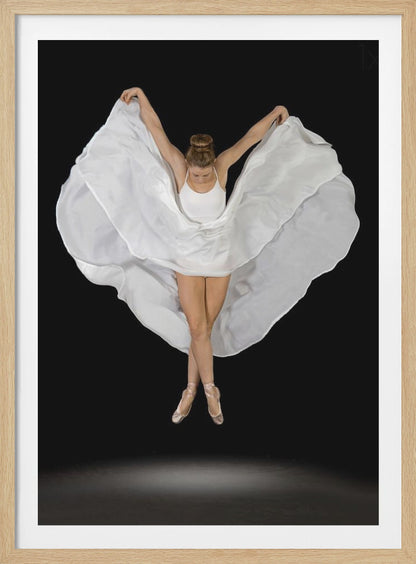 A high-angle studio photograph of a graceful ballet dancer suspended mid-air against a solid black background. She wears a white leotard and pointe shoes, with her legs crossed. Her arms are outstretched, holding a large, flowing white fabric that creates a shape like wings around her. Decor