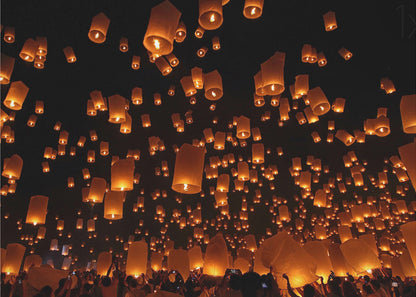 A framed photograph of a sky lantern festival at night, with hundreds of warm, orange-glowing lanterns floating up into the pitch-black sky from a crowd of people below. Artwork