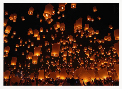A framed photograph of a sky lantern festival at night, with hundreds of warm, orange-glowing lanterns floating up into the pitch-black sky from a crowd of people below. Artwork