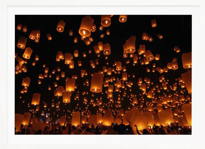 A framed photograph of a sky lantern festival at night, with hundreds of warm, orange-glowing lanterns floating up into the pitch-black sky from a crowd of people below. Artwork