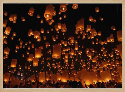 A framed photograph of a sky lantern festival at night, with hundreds of warm, orange-glowing lanterns floating up into the pitch-black sky from a crowd of people below. Artwork