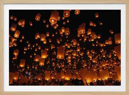 A framed photograph of a sky lantern festival at night, with hundreds of warm, orange-glowing lanterns floating up into the pitch-black sky from a crowd of people below. Artwork