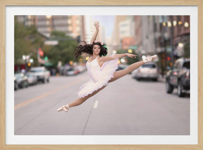 A ballerina in a white tutu and pointe shoes leaps into a split mid-air in the middle of a blurred city street, her arms extended gracefully. The image is set within a silver frame. Print