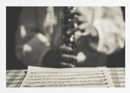 A shallow depth of field, black and white photograph focusing on sheet music in the foreground. The background is softly blurred, showing the hands of a musician holding a woodwind instrument. Wall Art