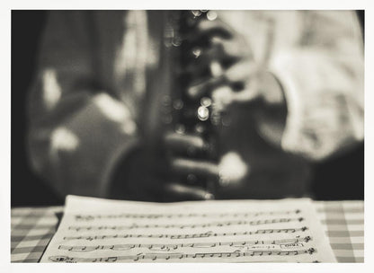 A shallow depth of field, black and white photograph focusing on sheet music in the foreground. The background is softly blurred, showing the hands of a musician holding a woodwind instrument. Wall Art