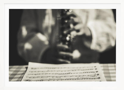 A shallow depth of field, black and white photograph focusing on sheet music in the foreground. The background is softly blurred, showing the hands of a musician holding a woodwind instrument. Wall Art