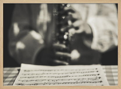 A shallow depth of field, black and white photograph focusing on sheet music in the foreground. The background is softly blurred, showing the hands of a musician holding a woodwind instrument. Wall Art