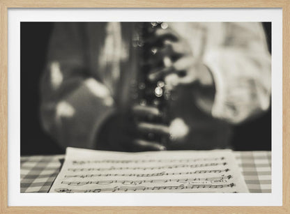 A shallow depth of field, black and white photograph focusing on sheet music in the foreground. The background is softly blurred, showing the hands of a musician holding a woodwind instrument. Wall Art