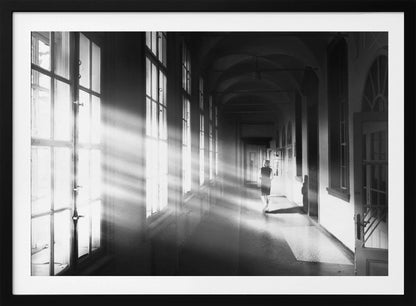 A black and white photograph of a woman walking away down a long, dark hallway. Bright shafts of sunlight pour through large windows on the left, creating a dramatic interplay of light and shadow on the floor and walls. Poster