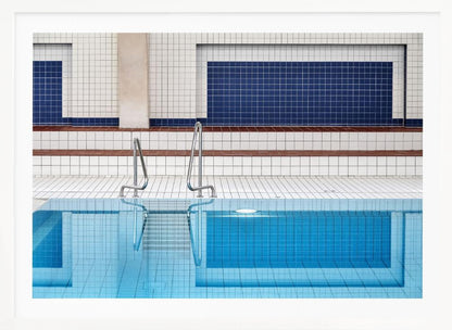 A framed, symmetrical photograph of a minimalist indoor swimming pool with blue and white tiles, stainless steel ladders, and a calm, reflective water surface. Poster