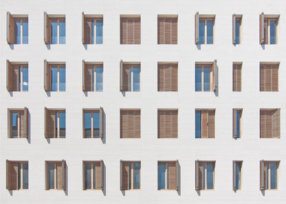 A symmetrical architectural photo of a modern white building facade featuring a grid of twenty-eight windows with wooden louvered shutters, some open and some closed, creating a varied pattern, all within a brushed silver frame. Decor