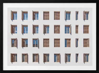 A symmetrical architectural photo of a modern white building facade featuring a grid of twenty-eight windows with wooden louvered shutters, some open and some closed, creating a varied pattern, all within a brushed silver frame. Decor