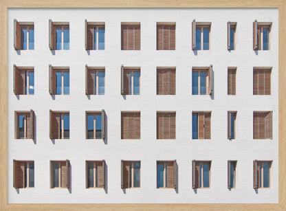 A symmetrical architectural photo of a modern white building facade featuring a grid of twenty-eight windows with wooden louvered shutters, some open and some closed, creating a varied pattern, all within a brushed silver frame. Decor