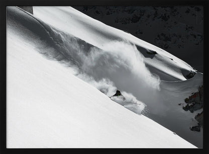 A dramatic black and white photograph of a skier speeding down a steep, snow-covered mountain, kicking up a large cloud of powder. The image is framed with a brushed silver border. Decor