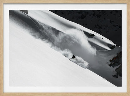 A dramatic black and white photograph of a skier speeding down a steep, snow-covered mountain, kicking up a large cloud of powder. The image is framed with a brushed silver border. Decor