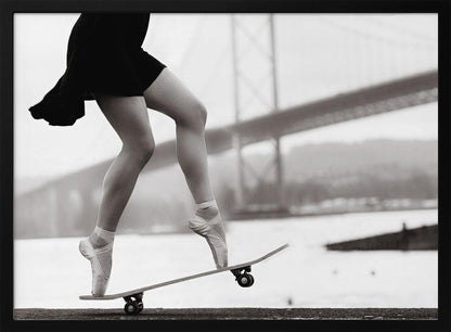 A black and white photograph of a ballerina's legs in a black dress, balancing en pointe on a skateboard with a blurred bridge in the background. Artwork