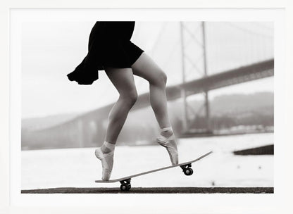 A black and white photograph of a ballerina's legs in a black dress, balancing en pointe on a skateboard with a blurred bridge in the background. Artwork